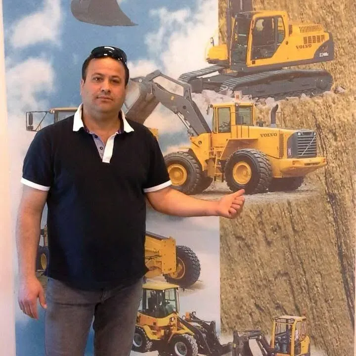 Ramez framför en vägg med grävmaskiner och hjullastare